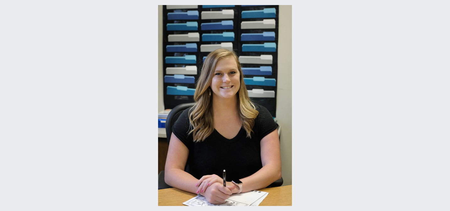 Girl sitting behind a desk with file folders hanging on the wall behind her